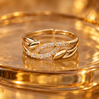 Ananta Leaf Infinity Sparkle Gold-Tone Ring on a honey amber glass backdrop