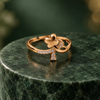 Titli Sparkle Butterfly Ribbon Rose Gold-Tone Ring on a forest green stone backdrop